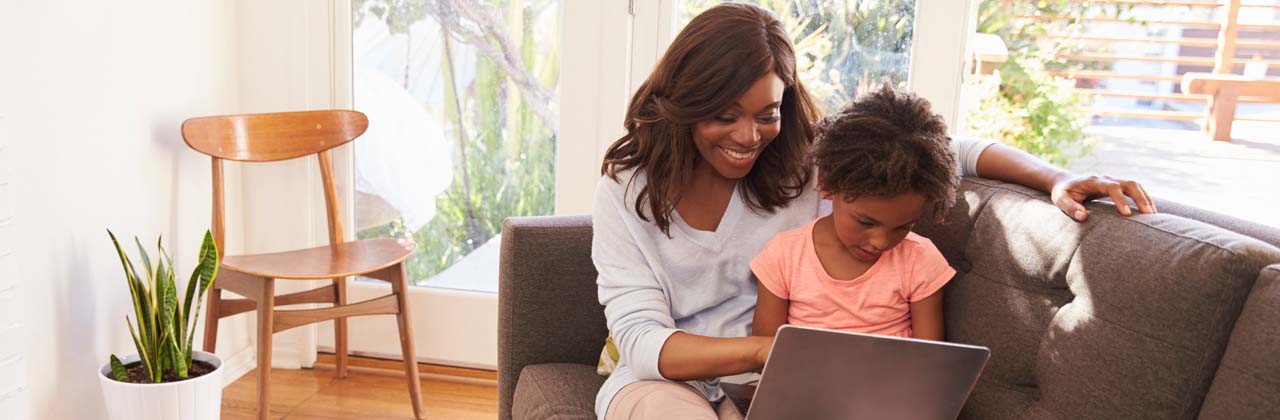 Mother and daughter sitting on couch looking at laptop 
