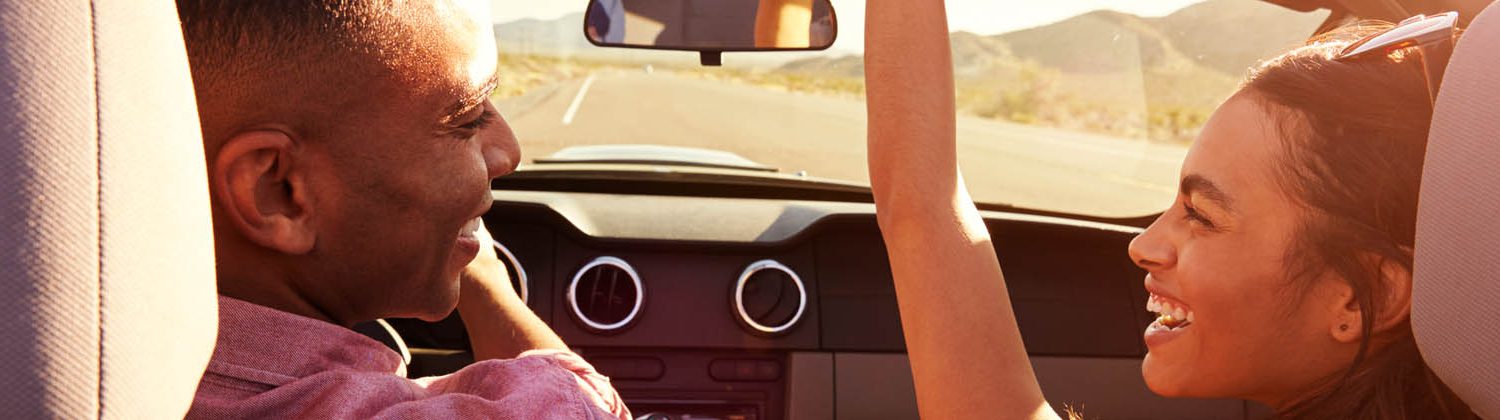 Man and woman driving in car on a sunny day and smiling