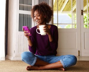 Woman looking at phone and smiling while holding coffee