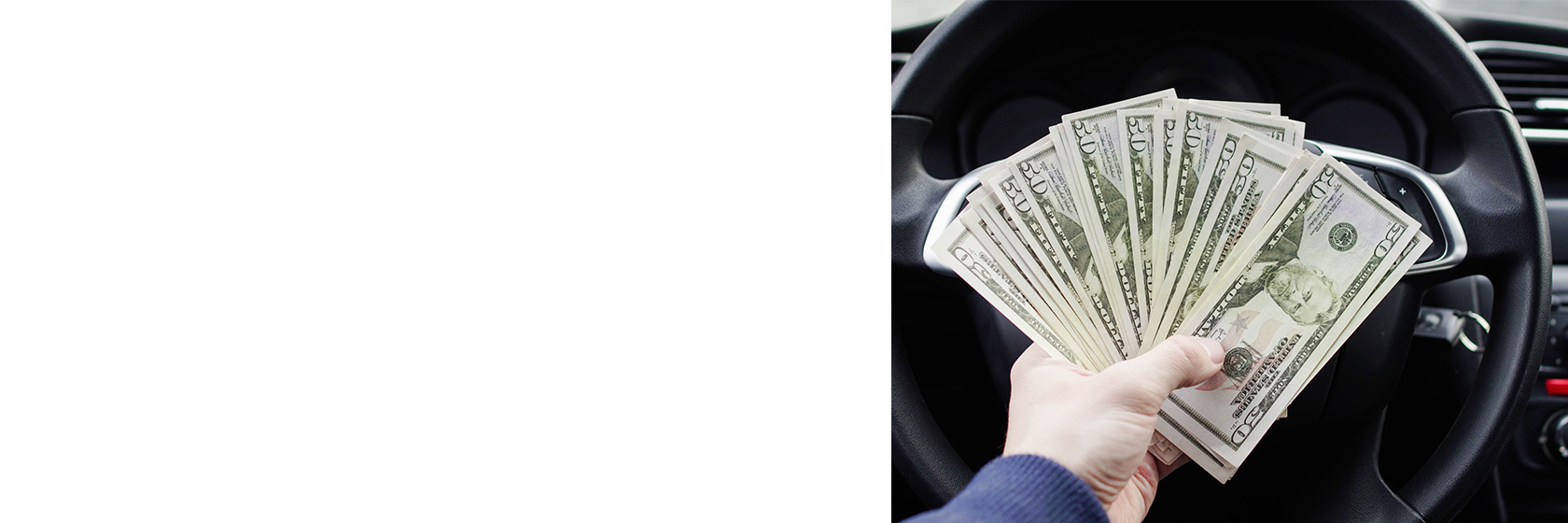 hand holding money in front of a car steering wheel