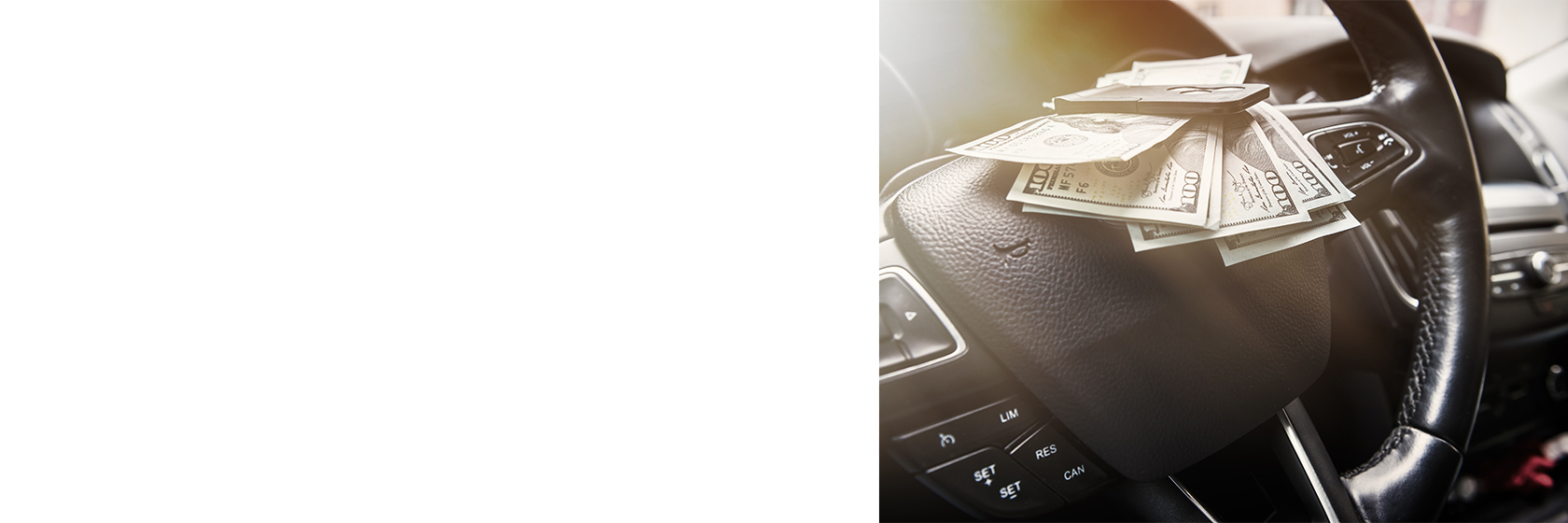 Image of a cars interior with money resting on the steering wheel.