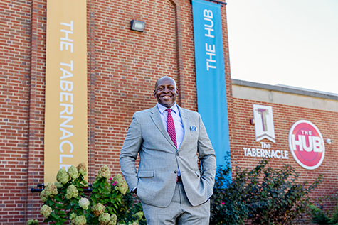 Image of a gentleman in a gray suit smiling in front of a church called "The Tabernacle"