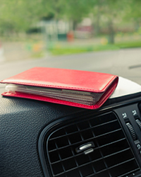 Image of a red wallet sitting atop a vehicle dashboard. 